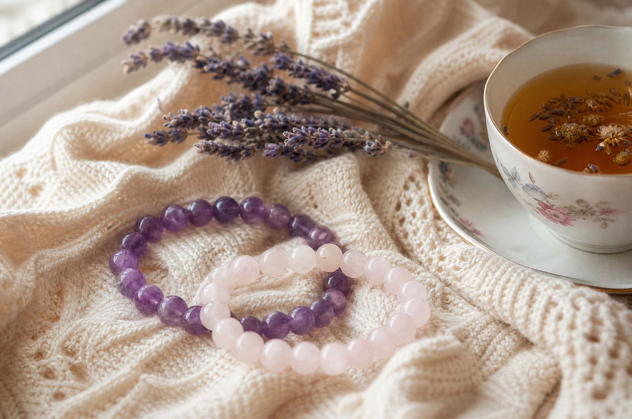 Bracelets en améthyste et quartz rose sur un châle en laine avec une tasse de tisane, cadeau fête des grands-mères